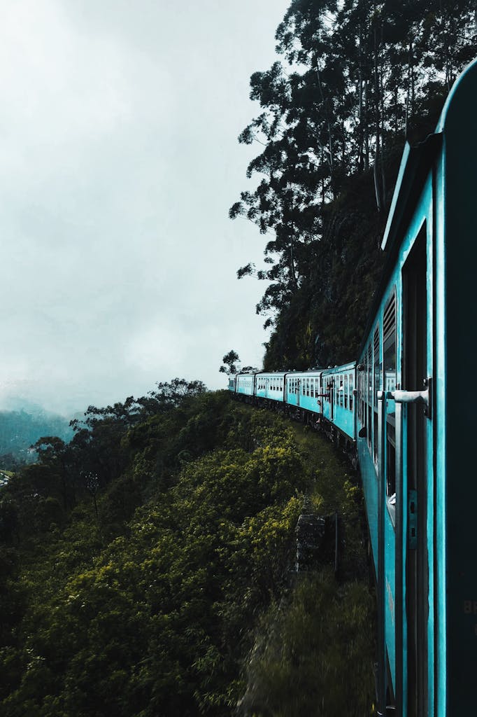 A vibrant train travels through breathtaking green hills and misty skies.