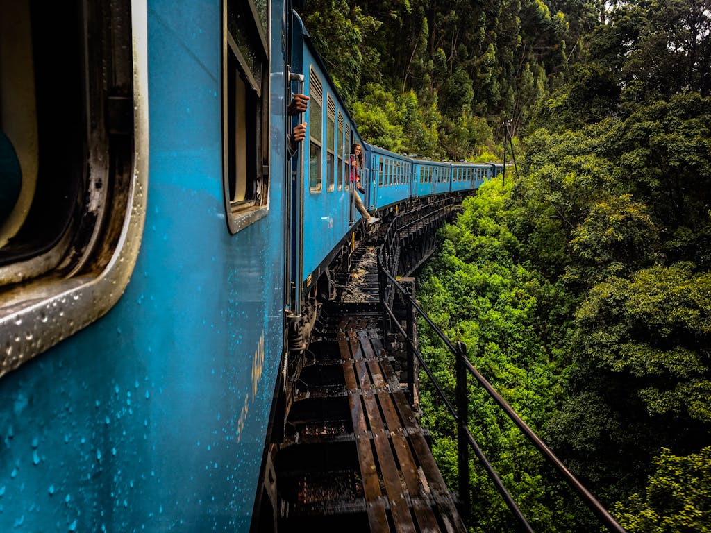 A vivid blue train travels through lush forests on an elevated track in Idalgashinna, Sri Lanka.