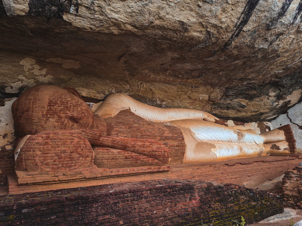 Ancient stone Reclining Buddha statue under rock shelter in Sigiriya, Sri Lanka.