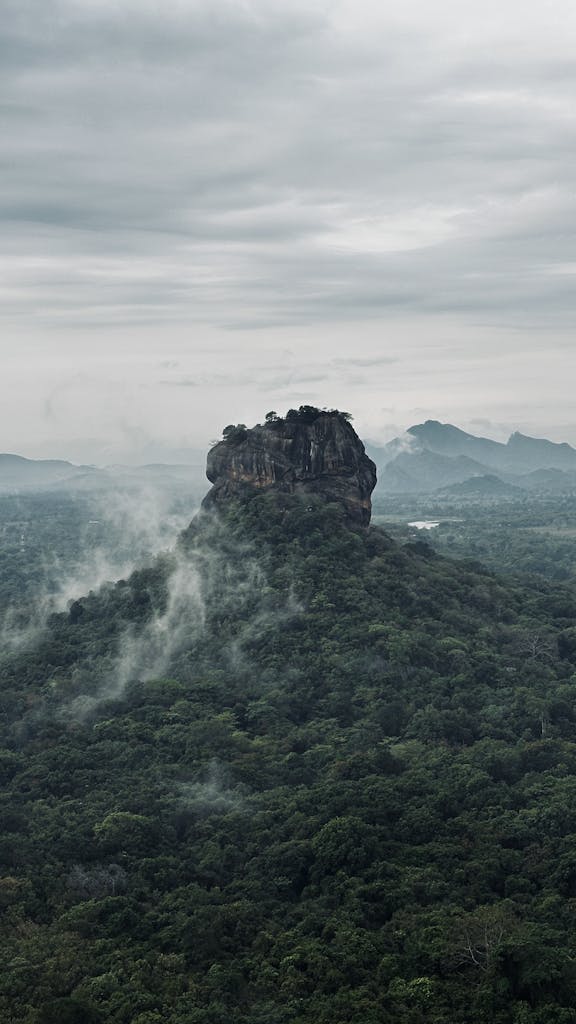 Dramatic aerial view of Sigiriya Rock, an iconic landmark in Sri Lanka surrounded by lush forest and mist.